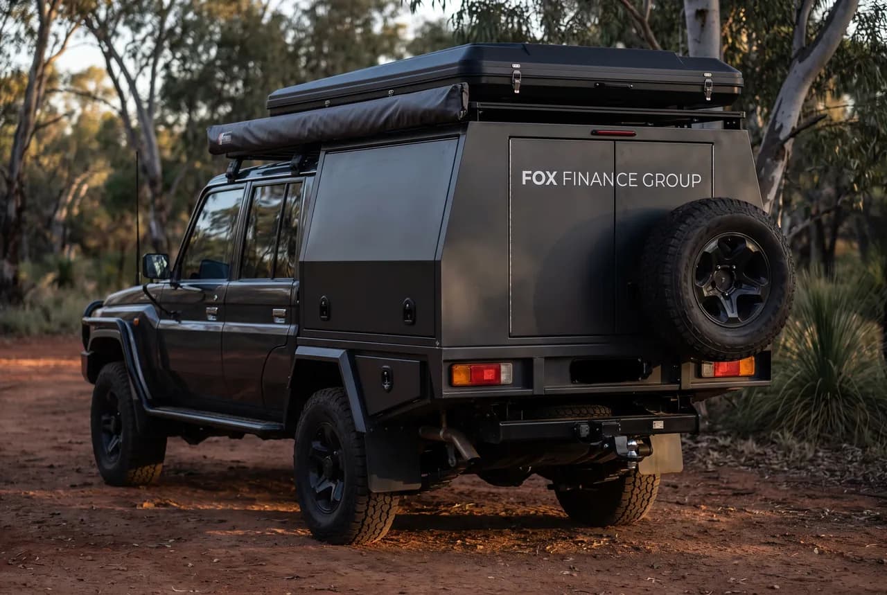 Close rear view of the black canopy and roof-top tent on a dark grey dual-cab 79 Series at a dusk bush camp, awning rolled, Fox Finance Group livery on the canopy door