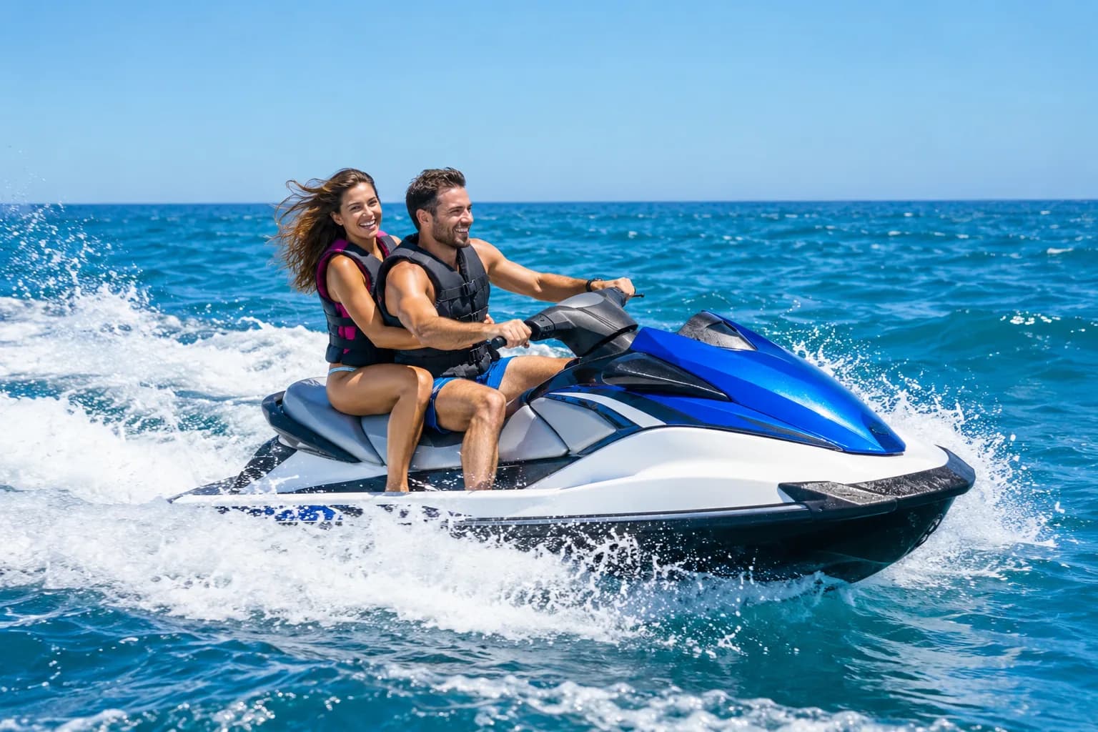 Two riders in life jackets laughing as they carve across open blue water on a blue and white jet ski